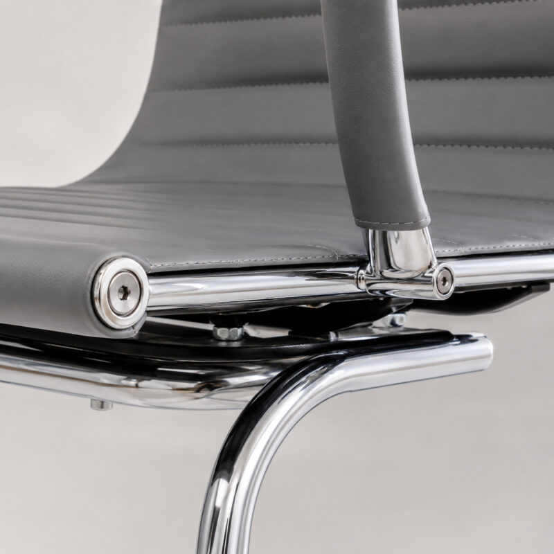 Detalhe estrutural da Cadeira Charles Eames cinza mostrando junção entre encosto, braço e estrutura cromada.