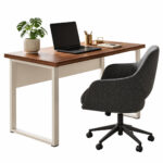 Mesa com tampo amadeirado e pés metálicos claros, acompanhada de notebook, planta e cadeira giratória estofada escura.