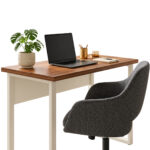 Mesa pé quadro com notebook, planta e materiais sobre o tampo, acompanhada de cadeira giratória estofada cinza.
