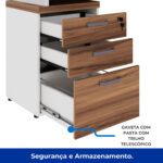Gavetas abertas do gaveteiro pedestal Gaveteiro pedestal com três gavetas abertas, frentes amadeiradas, puxadores metálicos e suportes para pasta suspensa na gaveta inferior.