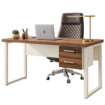 Mesa pé quadro com notebook e cadeira escura Mesa com duas gavetas fechadas, notebook e luminária dourada, acompanhada de cadeira escura com encosto matelassado.