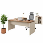 Mesa em L — composição de home office com notebook Mesa em L com notebook, cadeira com apoio de cabeça, planta e pequeno armário em composição de home office.