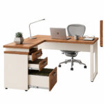 Mesa em L com gaveteiro — composição de home office Mesa em L com gaveteiro aberto, notebook, luminária e cadeira cinza, com pastas no compartimento inferior.