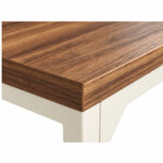 Mesa em L pé quadro — detalhe do canto e da estrutura Mesa em L pé quadro com detalhe do canto do tampo amadeirado e da estrutura metálica clara sob a borda.