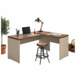 Mesa em L com notebook e banqueta em composição Mesa em L com notebook, luminária e acessórios sobre os tampos, acompanhada de banqueta e planta em vaso.