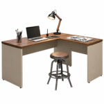 Mesa em L para Home Office em Goiânia — Composição com Acessórios Mesa em L com notebook, luminária e materiais sobre os tampos, acompanhada de banqueta no espaço central.