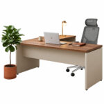 Mesa em L Sevilha e Champanhe com notebook, luminária e cadeira giratória com apoio de cabeça, acompanhada de planta.