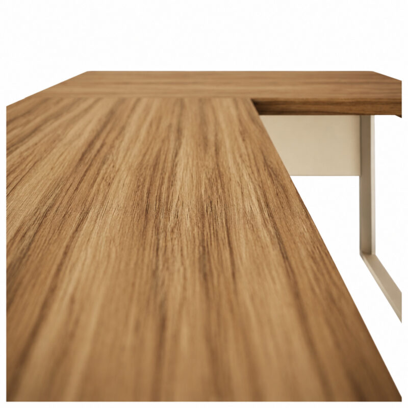 Vista aproximada ao longo do tampo amadeirado da mesa em L, com a junção das superfícies e um pé metálico ao fundo.