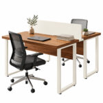 Estação dupla pé quadro — composição de home office duplo Estação dupla pé quadro com duas cadeiras pretas, notebook fechado, livros e vaso sobre os tampos amadeirados.