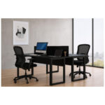 Mesa dupla preta ambientada com duas cadeiras de tela Mesa dupla preta com divisória, computador, notebook e duas cadeiras de tela em escritório com janela ampla.