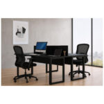 Mesa dupla preta para ambientes de trabalho em Goiás Mesa dupla preta com duas cadeiras de tela, monitor e notebook em escritório com janela ampla e piso amadeirado.