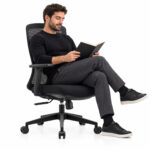 Cadeira giratória em tela preta — em uso com notebook Pessoa sentada em cadeira de escritório preta com encosto em tela, utilizando um notebook.